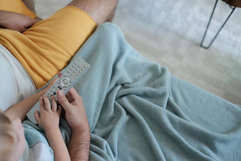 Father and son are watching Tv together, holding the remote control in their hands, cosy home atmosphere royalty free stock image Father and son are watching Tv together, holding the remote control in their hands, cosy home atmosphere royalty free stock image