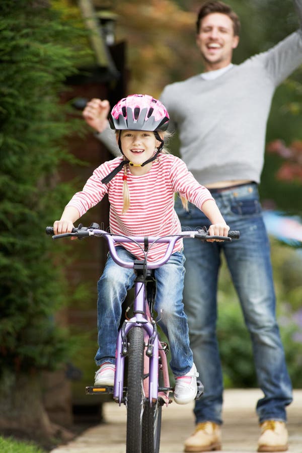 Father Teaching Daughter To Ride Bike In Garden