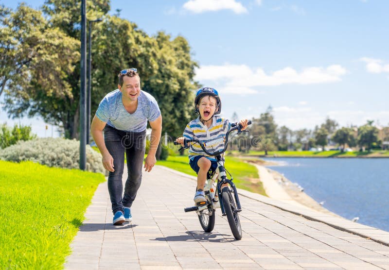 Father teaching his son to ride a bike and having fun together at the park