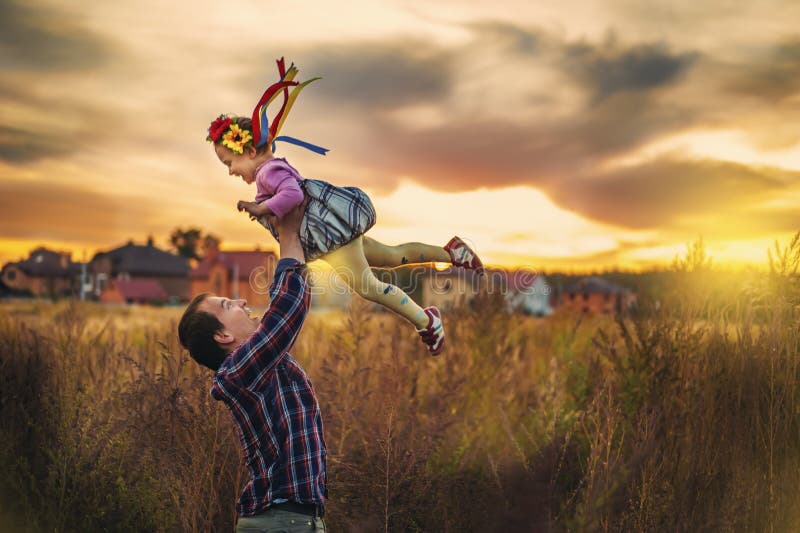 Father throws up his daughter in sunset time. Child fly in sky. Fatherhood and happy childhood. Girl in ukrainian wreath on head.