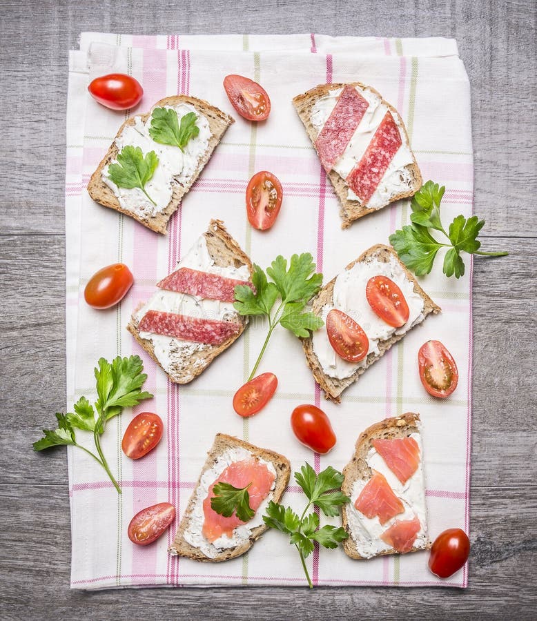 Fatia de pão de centeio fresco com queijo creme com peixes, os tomates de cereja e salsa vermelhos do salame em uma toalha de mes imagens de stock Fatia de pão de centeio fresco com queijo creme com peixes, os tomates de cereja e salsa vermelhos do salame em uma toalha de mes imagens de stock
