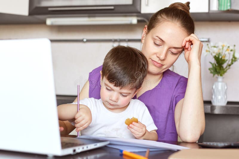 Fatigue overworked young female enterpreneur involved in family business, tries to make financial report, takes care of child simu royalty free stock photos Fatigue overworked young female enterpreneur involved in family business, tries to make financial report, takes care of child simu royalty free stock photos