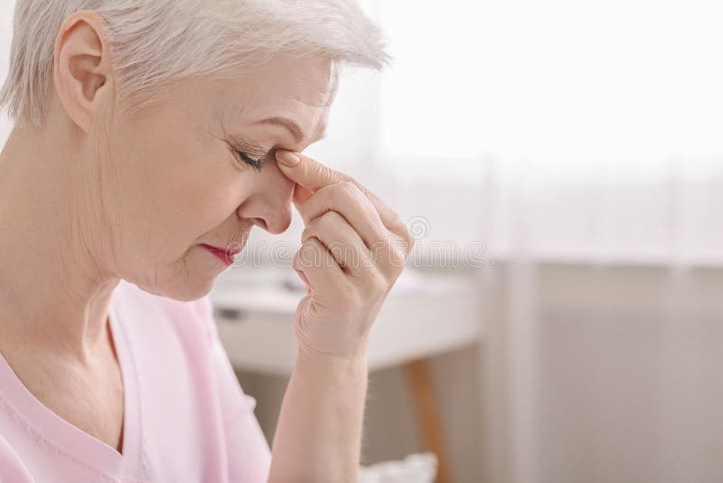 Fatigued senior woman massaging nose bridge, feeling eye strain or headache trying to relieve pain, thinking of problems, empty space