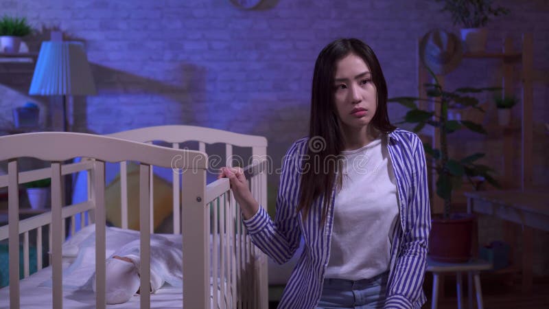 Fatigué triste jeune asiatique maman roche un lit bébé