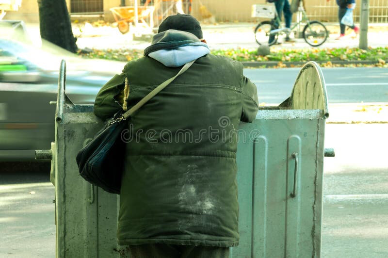 Poor and hungry homeless man in dirty clothes looking for food in the dumpster on the urban street in the city. Poor and hungry homeless man in dirty clothes looking for food in the dumpster on the urban street in the city