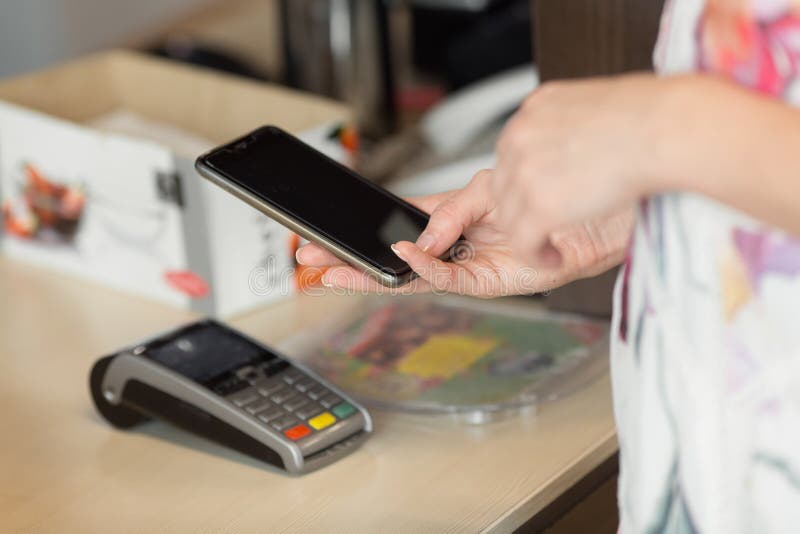 Fattura di pagamento della donna tramite lo smartphone facendo uso di tecnologia del nfc in caffè immagine stock Fattura di pagamento della donna tramite lo smartphone facendo uso di tecnologia del nfc in caffè immagine stock