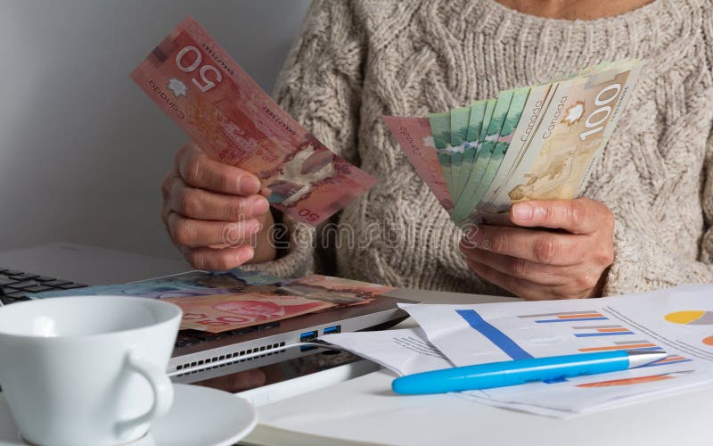 Fatture dei contanti da valuta canadese Dollari Donna anziana che conta le fatture sulla tavola fotografia stock Fatture dei contanti da valuta canadese Dollari Donna anziana che conta le fatture sulla tavola fotografia stock