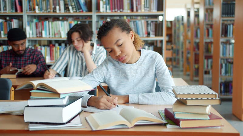 Fată americană obosită studiind în biblioteca universitară scriind cărți stock video