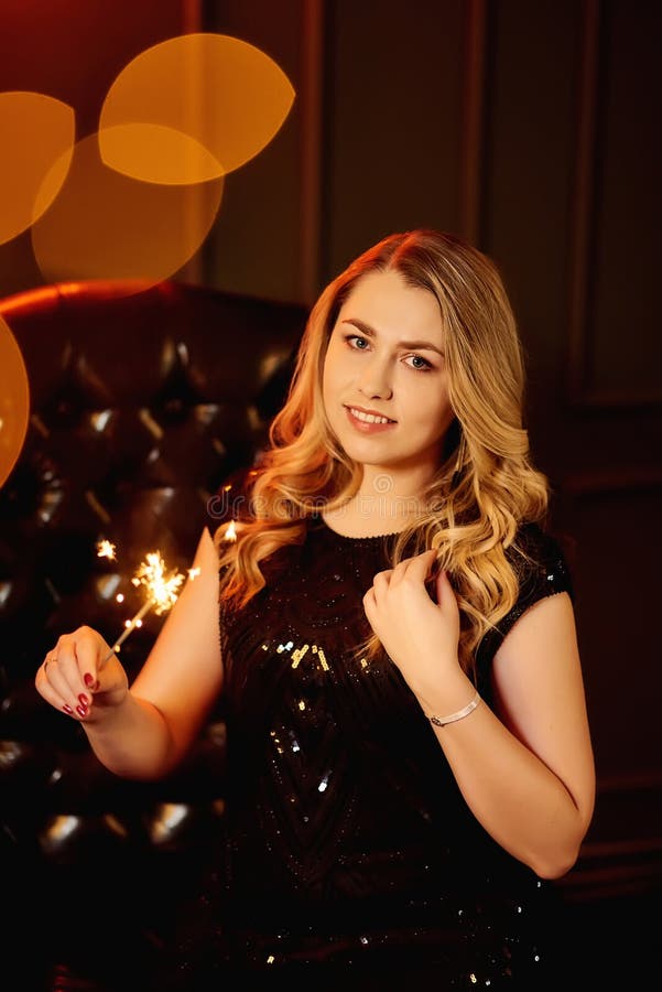 Fată blondă zâmbitoare într-o rochie neagră ține un foc bengali stock image