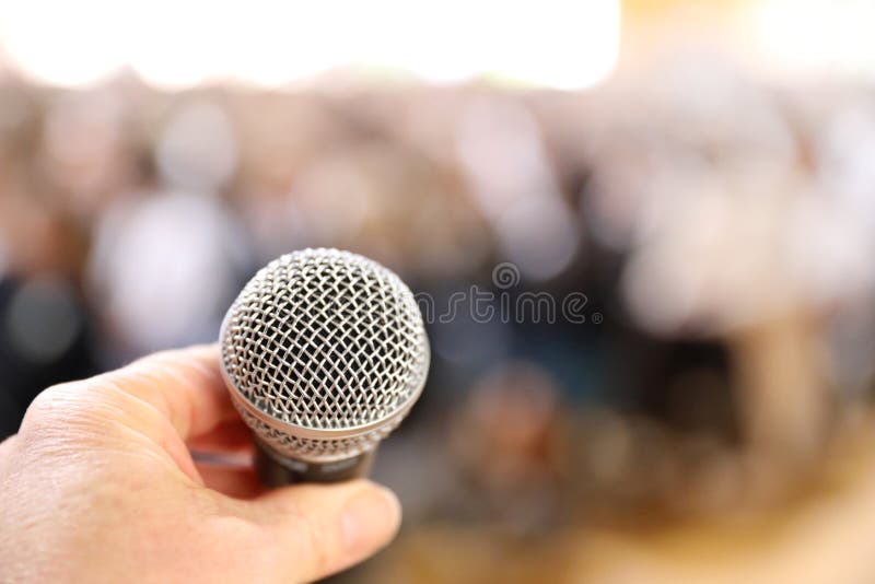 Fear of public speaking. A very close microphone in front of a blurred crowd royalty free stock image
