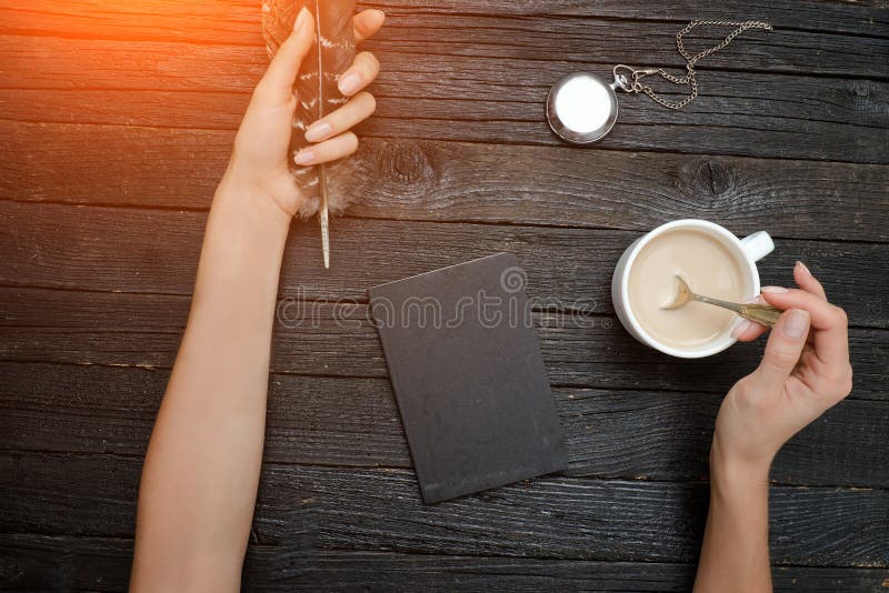 Feather and cup of coffee in a female hand, notebook and clock. stock photography