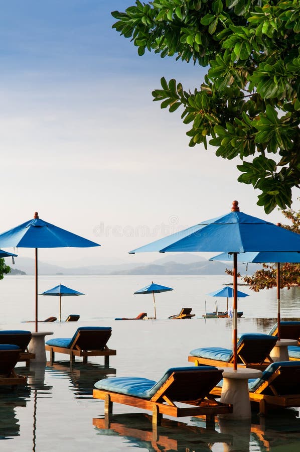 FEB 6, 2013 Phuket, Thailand - Resort style Vacation Relaxation resort beach bed under blue umbrella in infinity pool tropical sea view at evening time. FEB 6, 2013 Phuket, Thailand - Resort style Vacation Relaxation resort beach bed under blue umbrella in infinity pool tropical sea view at evening time