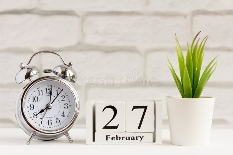 27 februari op een houten kalender naast de wekker Kalenderdatum, vakantiegebeurtenis of verjaardag