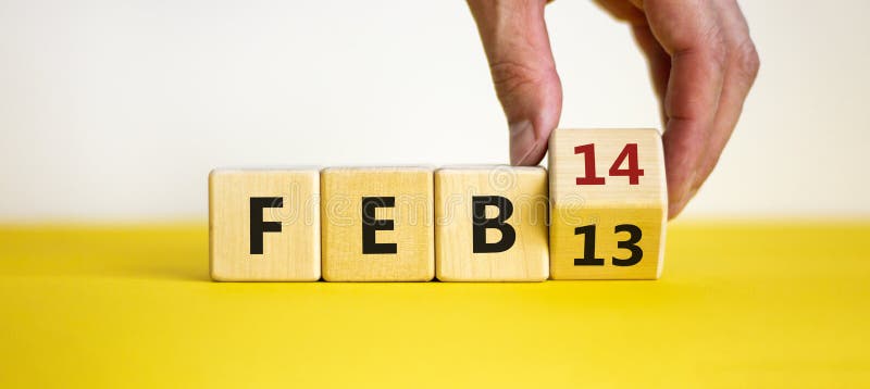 February 14 valentines day symbol. Hand turns the cube and changes the word `Feb 13` to `Feb 14`. Beautiful yellow table, white background, copy space. February 14 Valentines day concept. February 14 valentines day symbol. Hand turns the cube and changes the word `Feb 13` to `Feb 14`. Beautiful yellow table, white background, copy space. February 14 Valentines day concept.