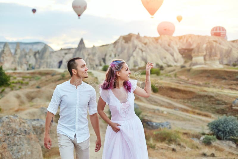 Fecha de un par en amor en la puesta del sol contra el fondo de globos en Cappadocia, Turquía Hombre y mujer que abrazan la coloc imagen de archivo libre de regalías Fecha de un par en amor en la puesta del sol contra el fondo de globos en Cappadocia, Turquía Hombre y mujer que abrazan la coloc imagen de archivo libre de regalías