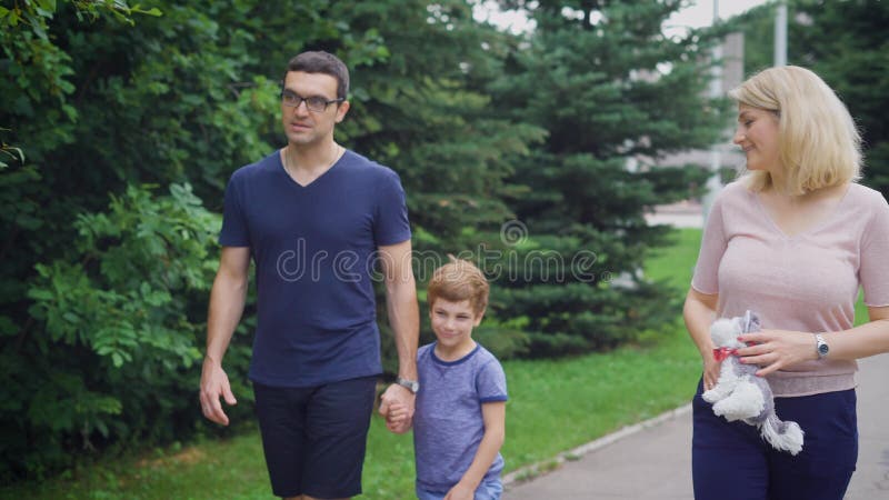 Feche acima da família feliz que anda junto no riso da rua Pai e mãe que falam entre si e filho