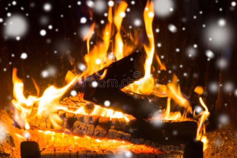 Winter, christmas, warmth, fire and coziness concept - close up of firewood burning in fireplace with snow. Winter, christmas, warmth, fire and coziness concept - close up of firewood burning in fireplace with snow