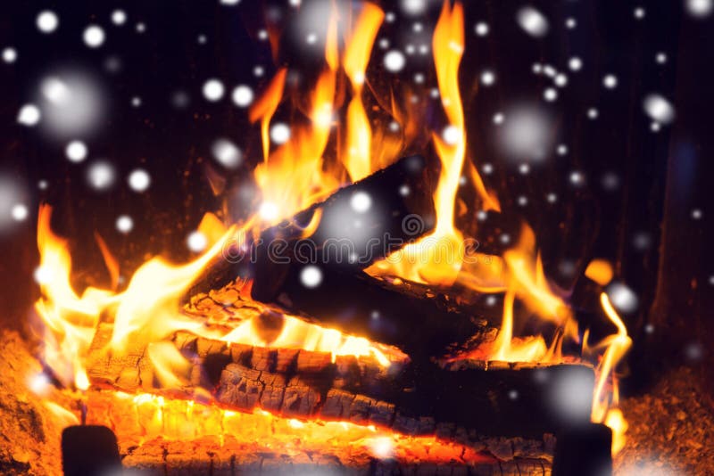 Winter, christmas, warmth, fire and coziness concept - close up of firewood burning in fireplace with snow. Winter, christmas, warmth, fire and coziness concept - close up of firewood burning in fireplace with snow