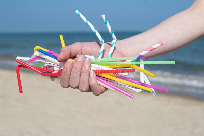 Feche acima da mão que guarda as palhas plásticas que poluem a praia