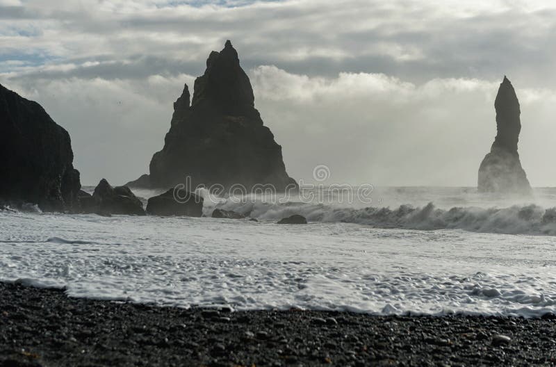 Feche acima da praia preta Reynisfjara da areia em Islândia Rochas na água Ondas de oceano Manhã ventosa imagens de stock Feche acima da praia preta Reynisfjara da areia em Islândia Rochas na água Ondas de oceano Manhã ventosa imagens de stock