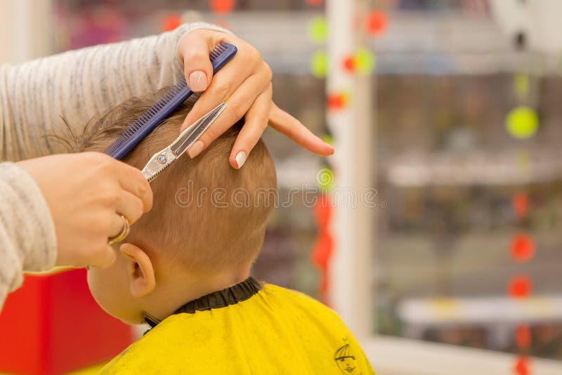 Feche acima das m?os do cabeleireiro A mulher ? estando e de fatura o corte de cabelo para o menino pequeno Est? guardando um pen fotografia de stock Feche acima das m?os do cabeleireiro A mulher ? estando e de fatura o corte de cabelo para o menino pequeno Est? guardando um pen fotografia de stock