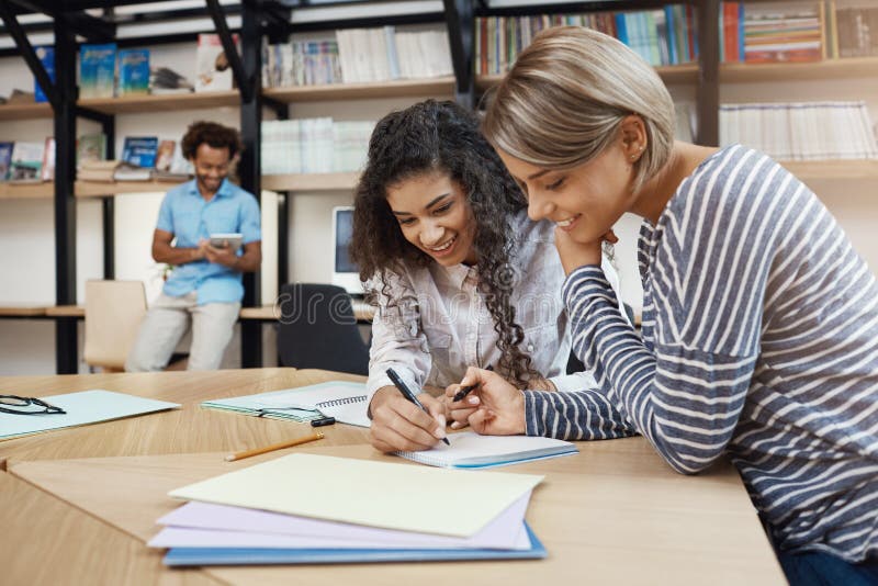 Feche acima das meninas multi-étnicas novas bonitas do estudante dos pares que fazem trabalhos de casa junto, escrevendo o ensaio imagem de stock Feche acima das meninas multi-étnicas novas bonitas do estudante dos pares que fazem trabalhos de casa junto, escrevendo o ensaio imagem de stock