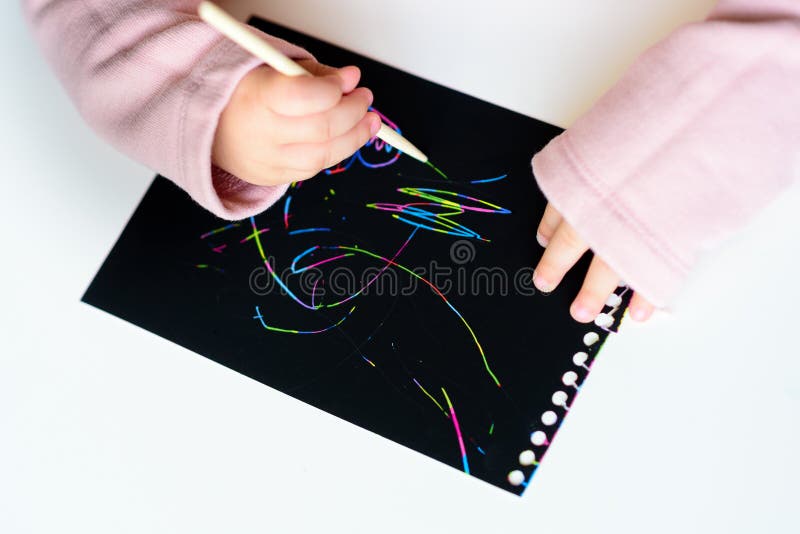 Feche acima das mãos de um desenho da criança pequena no papel de pintura do risco mágico com vara do desenho fotos de stock Feche acima das mãos de um desenho da criança pequena no papel de pintura do risco mágico com vara do desenho fotos de stock