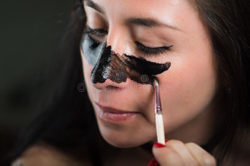 Feche acima de uma jovem mulher da beleza que aplying em sua cara uma máscara preta para limpar a pele foto de stock royalty free Feche acima de uma jovem mulher da beleza que aplying em sua cara uma máscara preta para limpar a pele foto de stock royalty free