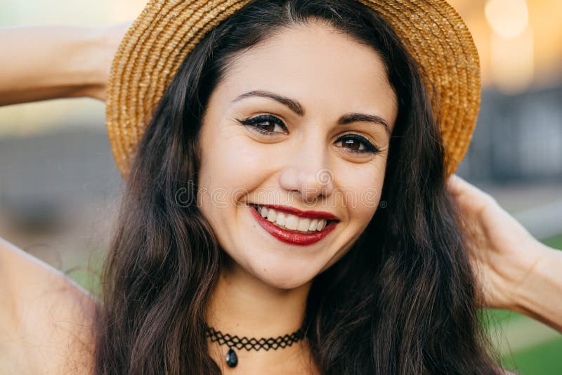 Feche acima do retrato da fêmea bonito com o cabelo escuro, os olhos encantadores e o chapéu vestindo do verão da palha do sorris foto de stock Feche acima do retrato da fêmea bonito com o cabelo escuro, os olhos encantadores e o chapéu vestindo do verão da palha do sorris foto de stock