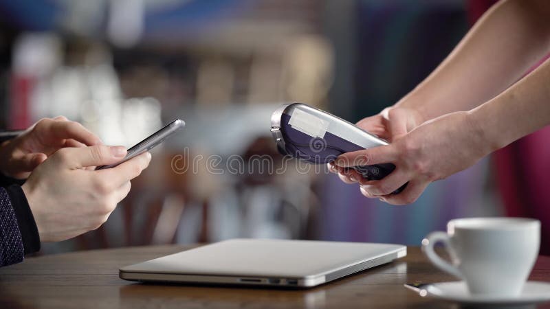 Feche acima do tiro da mão do ` s do garçom, que aceita o pagamento para o jantar no restaurante usando a aplicação no móbil