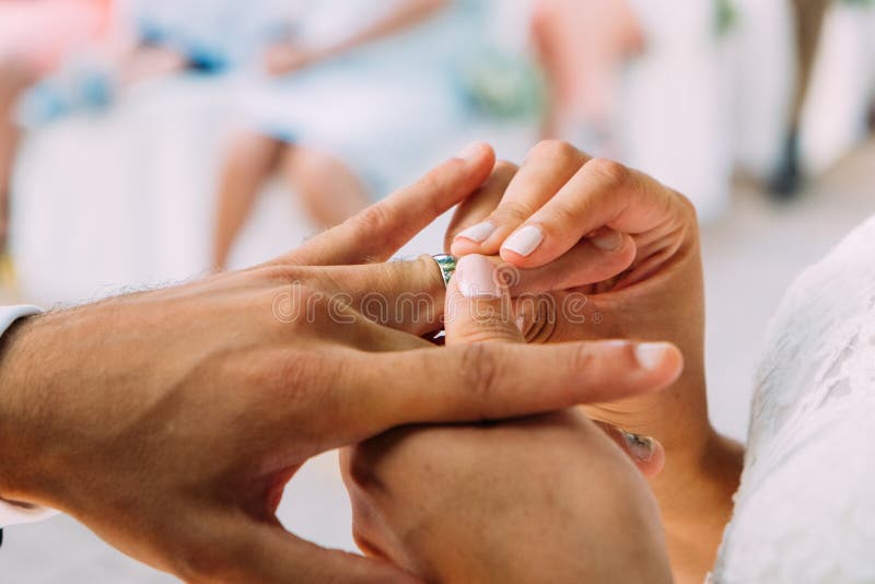 Feche acima dos pares de novo weds recentemente com as mãos da mulher que põem a aliança de casamento do ouro nos dedos do marido imagens de stock Feche acima dos pares de novo weds recentemente com as mãos da mulher que põem a aliança de casamento do ouro nos dedos do marido imagens de stock