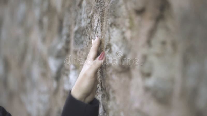 Feche acima em parede de pedra tocante da mão da mulher