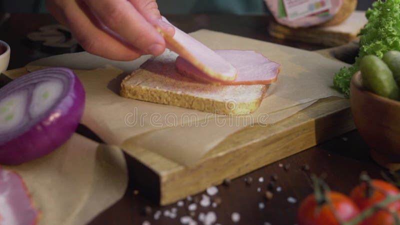 Feche acima o vídeo de fazer o sanduíche com presunto cortado e os vegetais, cozinheiro chefe adicionam o presunto fumado ao sand