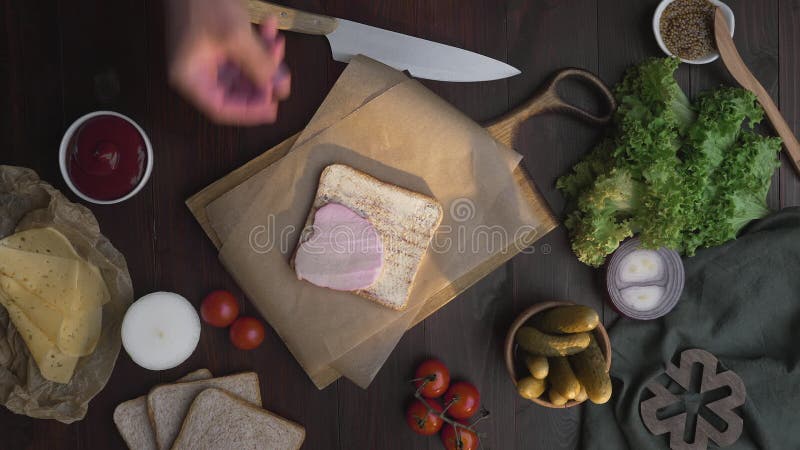 Feche acima o vídeo de fazer o sanduíche com presunto cortado e os vegetais, cozinheiro chefe adicionam o presunto fumado ao sand
