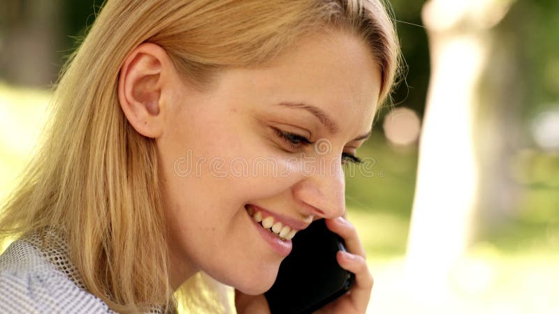 Feche a alegre mulher caucasiana segurando celular sobre a natureza. jovem mulher falando com o smartphone.