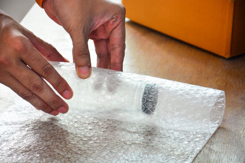 Feche as mãos de um cara usando o invólucro de bolhas para embalar um frasco de vidro antes de colocá-lo na caixa de papelão e en