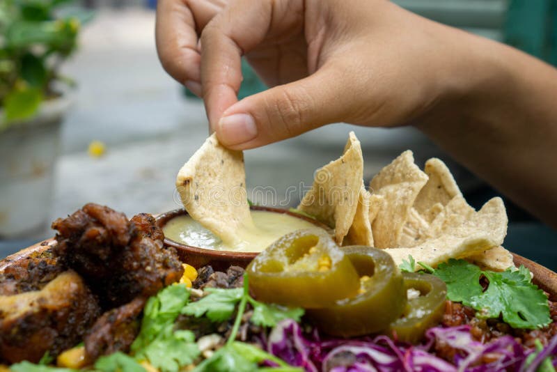 Feche a foto de comida de uma pessoa mergulhando um chip tortilla em molho de mostarda de mel com uma taça de salada mista com fra fotos de stock royalty free