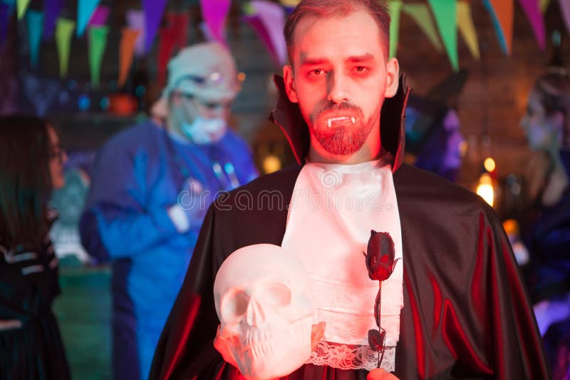 Homem vestido com fantasia de drácula para o halloween, olhando para um  crânio humano. homem com dentes de vampiro. homem assustador com fantasia  de halloween.