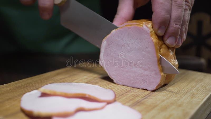 Feche o vídeo do presunto natural saboroso é cortado acima pela faca afiada na placa de madeira, carne fumado espasmódica, fazend