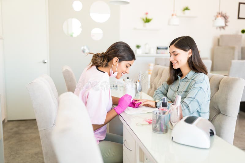 Smiling manicurist decorating nails with color on client`s hand at beauty spa. Smiling manicurist decorating nails with color on client`s hand at beauty spa