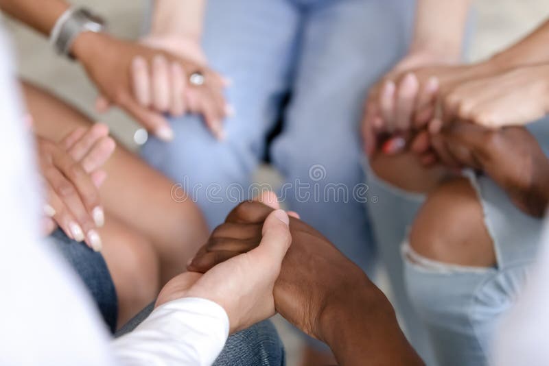 Close up of multiracial people sit in circle holding hands show mutual support and understanding at therapy session, diverse men and women gather give help at group psychological treatment. Close up of multiracial people sit in circle holding hands show mutual support and understanding at therapy session, diverse men and women gather give help at group psychological treatment