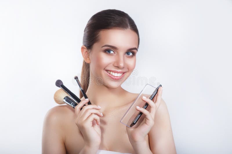 Fecho de uma linda jovem e sorridente modelo feminino com escovas cosméticas e sombra ocular sobre fundo branco imagem de stock royalty free Fecho de uma linda jovem e sorridente modelo feminino com escovas cosméticas e sombra ocular sobre fundo branco imagem de stock royalty free