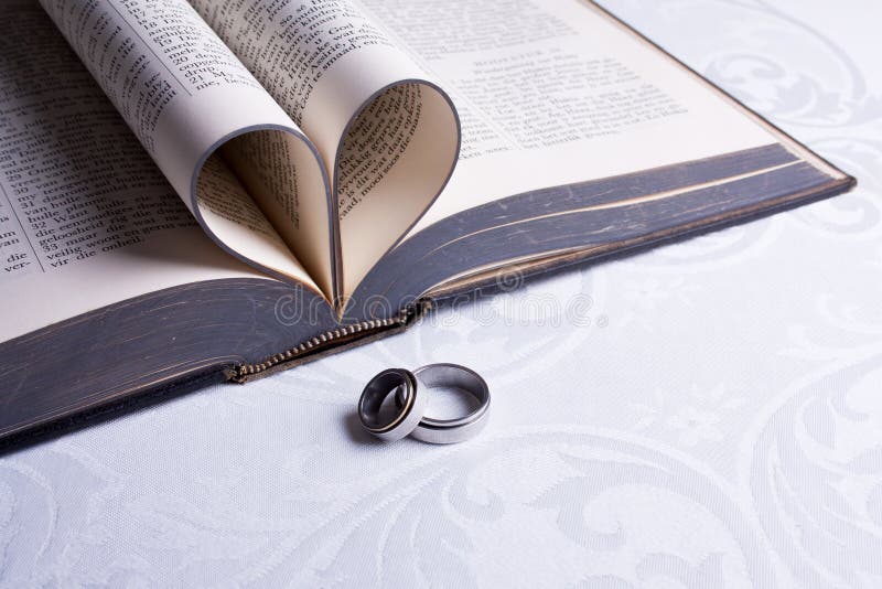 Two wedding rings with Hebrew on them and an open Afrikaans Bible with pages folded in a heart. Two wedding rings with Hebrew on them and an open Afrikaans Bible with pages folded in a heart