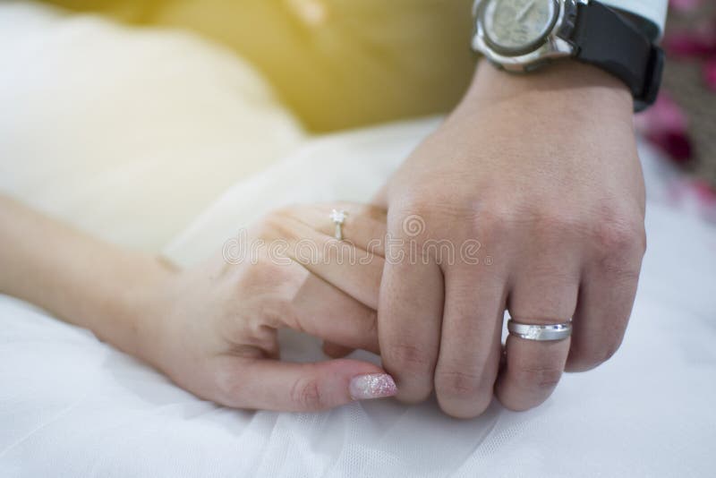 Fedi nuziali sulle mani dello sposo e della sposa coppie impegnate che si tengono per mano con il diamante e l'anello d'argento immagine stock Fedi nuziali sulle mani dello sposo e della sposa coppie impegnate che si tengono per mano con il diamante e l'anello d'argento immagine stock