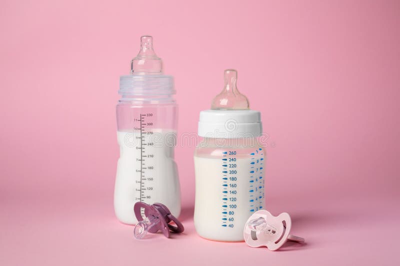 Feeding Bottles with Milk and Baby Pacifiers on Pink Background Stock