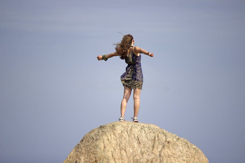 Una giovane donna si erge su una roccia con il vento tra i capelli di sentirsi potente.