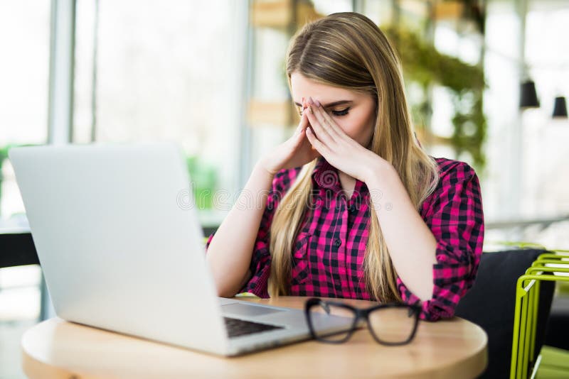 Feeling tired and stressed. Frustrated young woman keeping eyes closed and massaging nose while sitting at her working place in of stock photography Feeling tired and stressed. Frustrated young woman keeping eyes closed and massaging nose while sitting at her working place in of stock photography