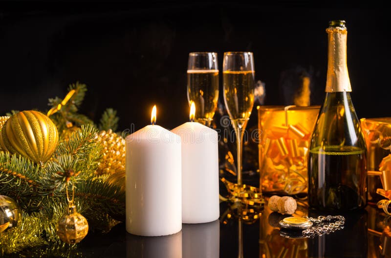 Festive Christmas still life with champagne in a bottle and flutes, burning white candles and golden gifts and baubles over a dark background. Festive Christmas still life with champagne in a bottle and flutes, burning white candles and golden gifts and baubles over a dark background