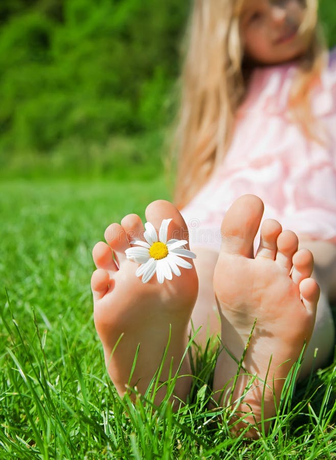 Child Feet with Daisy Flower on Green Grass in a Summer Park. Stock