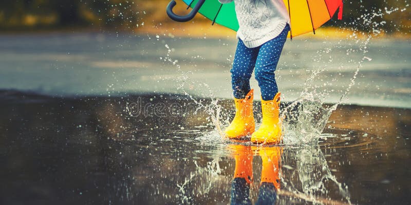 Feet of child in yellow rubber boots jumping over a puddle in the rain